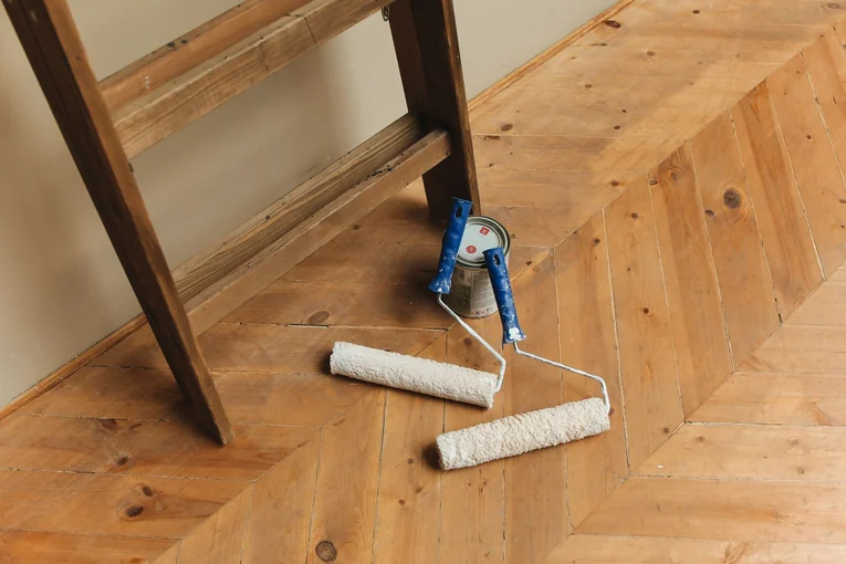 Paint rollers and ladder on a wooden floor, perfect for DIY renovation projects.