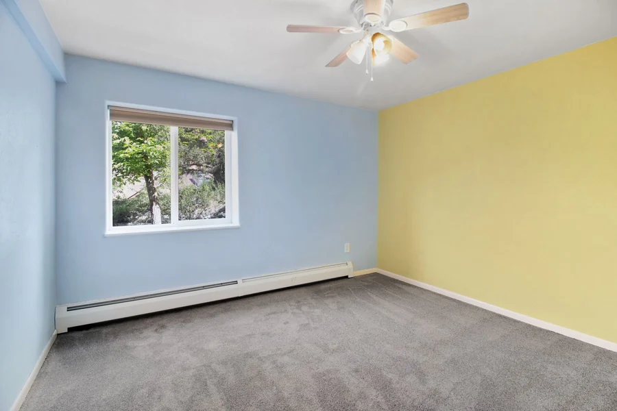 Bright, empty room with blue and yellow walls, carpet, and window view.