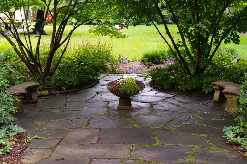 Peaceful stone patio surrounded by greenery and a central plant centerpiece in a New York garden.